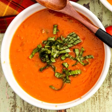 Roasted tomato and basil soup in a white bowl with a wooden soup spoon.