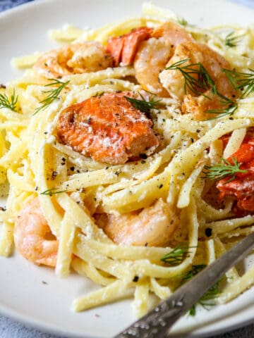 Shrimp and salmon alfredo pasta on a white plate.