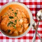 A bowl of soup on a plate, with two spoons