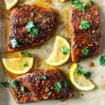 Three Cajun honey butter salmon fillets with lemon wedges.
