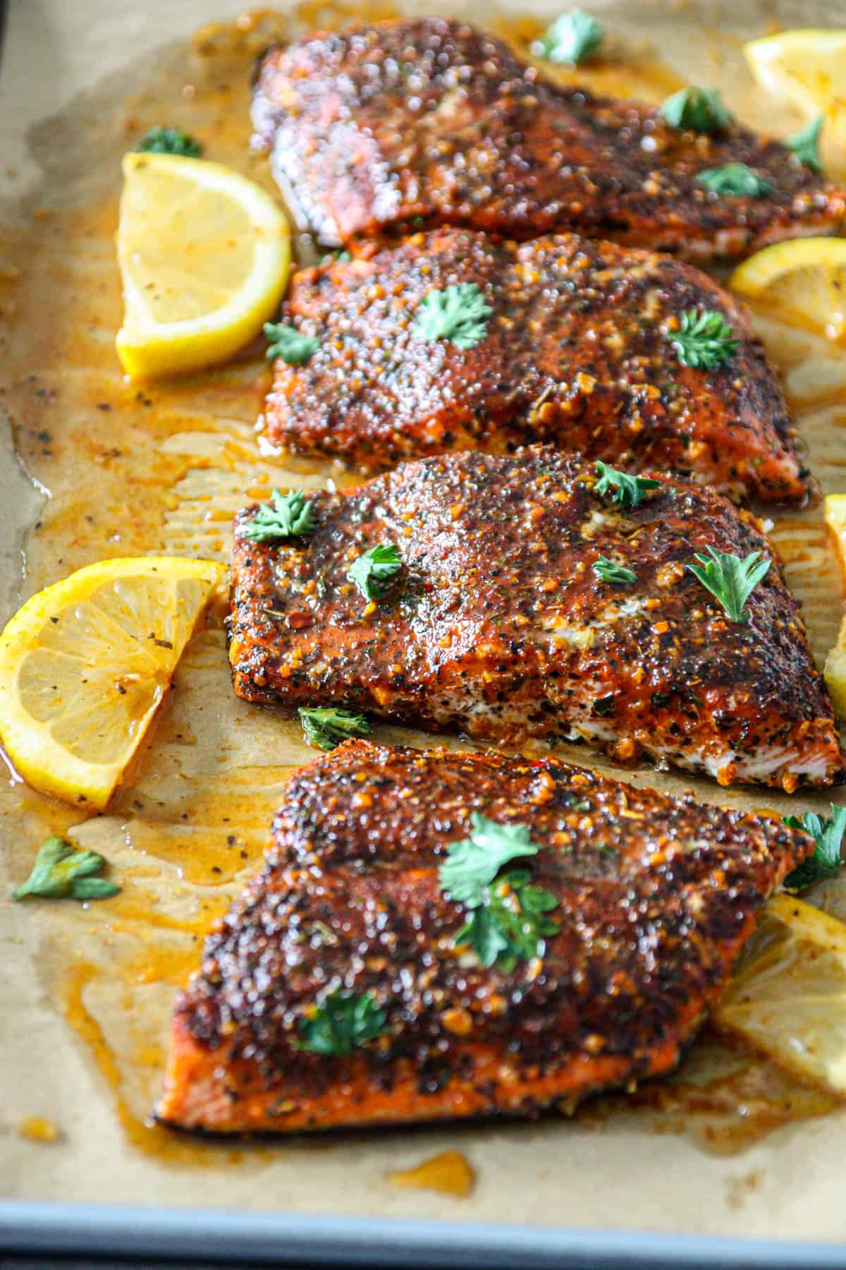 Four baked Cajun honey butter salmon fillets on a baking sheet.