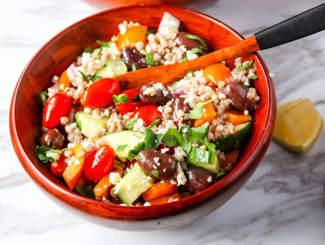 Grains and vegetables in a wooden bowl sitting on a marble counter top.