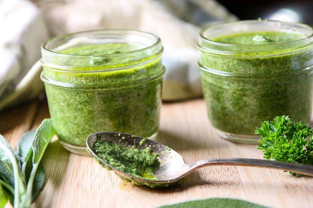 A jar of pesto on a cutting board with a spoon