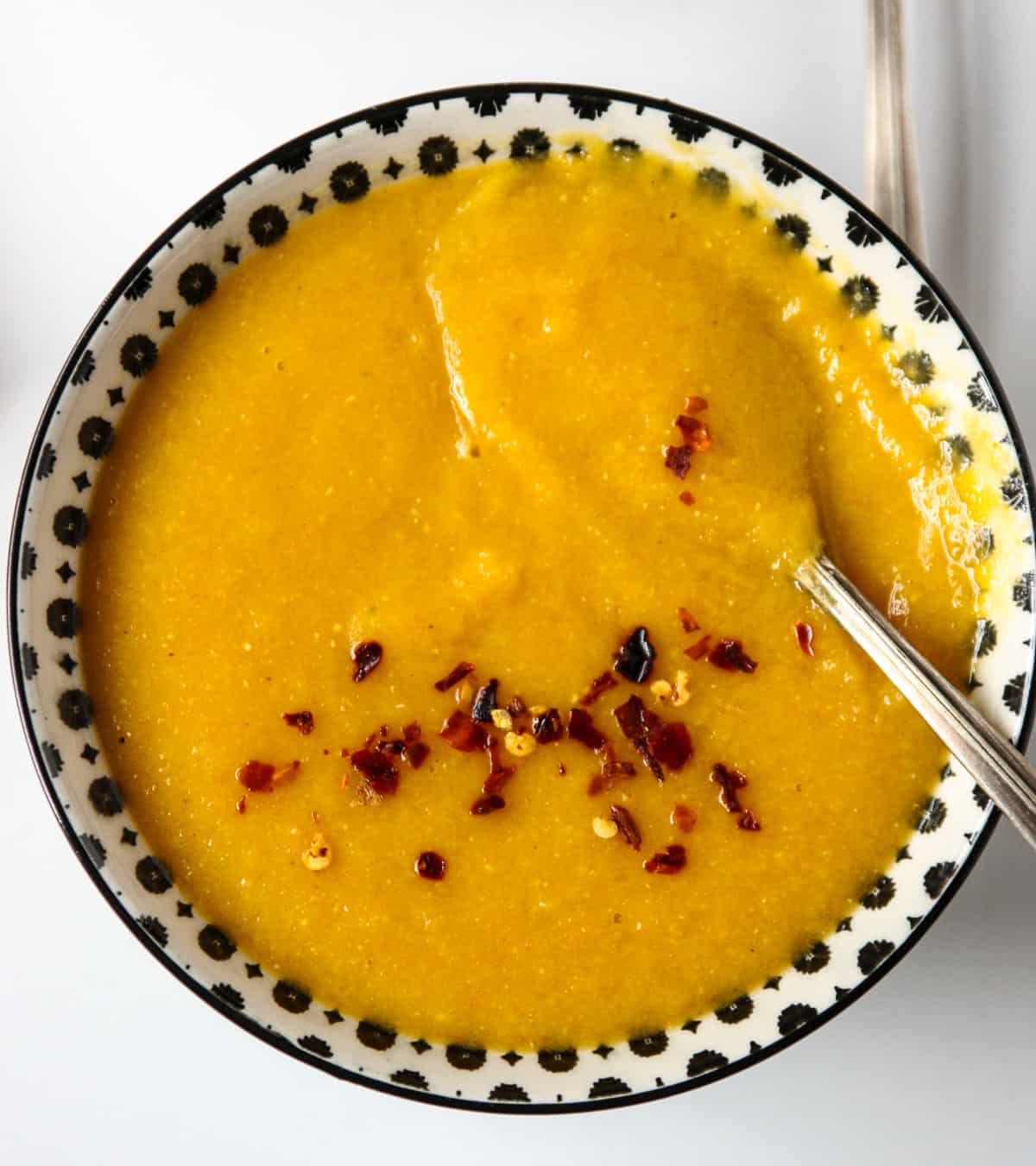 Carrot lentil soup in a black and white bowl with a spoon dipping in.