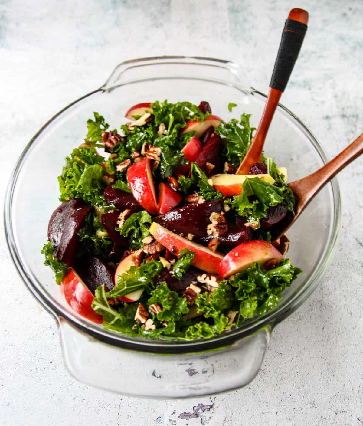 Kale and beet salad with apples in a glass bowl with wooden salad forks.