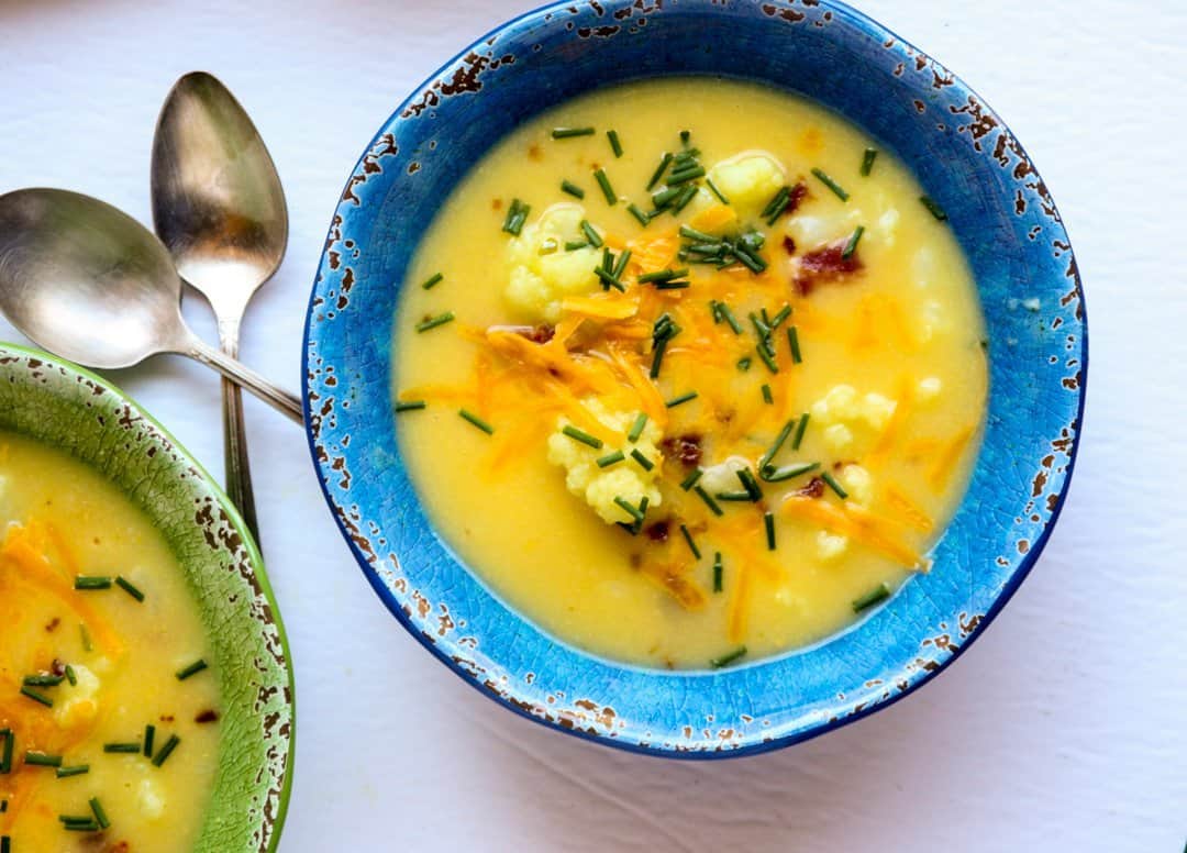 Two bowls of soup in blue and green bowls on a white table.