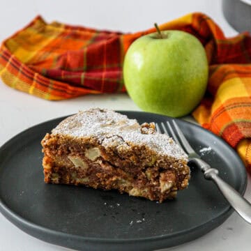 A slice of apple walnut cake on a black plate.