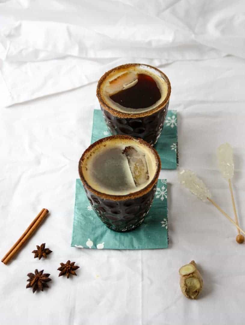 Two cocktails in glasses on blue napkins, sitting on top of a white table with cinnamon pieces nearby