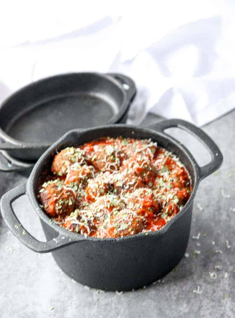 Top shot of meatless mushroom meatballs in marinara sauce, topped with parmesan cheese in black pot