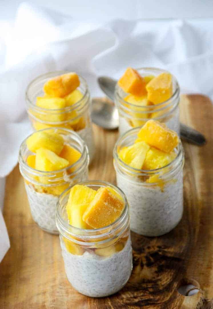 Five half pint jars of coconut chia pudding topped with mango and pineapple.
