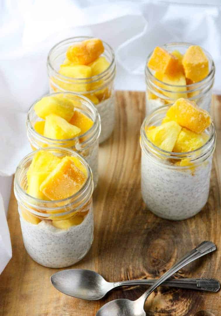 Four glass jars filled with coconut chia pudding and fruit.