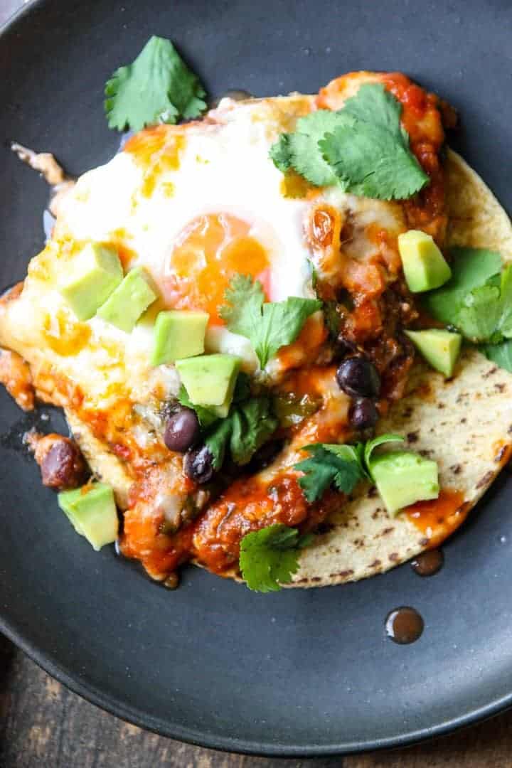 Fried Eggs and sauce on a tortilla on a black plate.