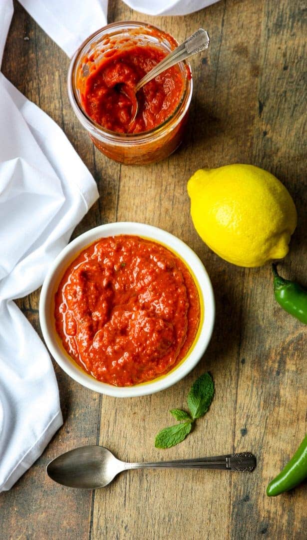 A bowl of hot sauce sitting on top of a wooden table, with with a lemon
