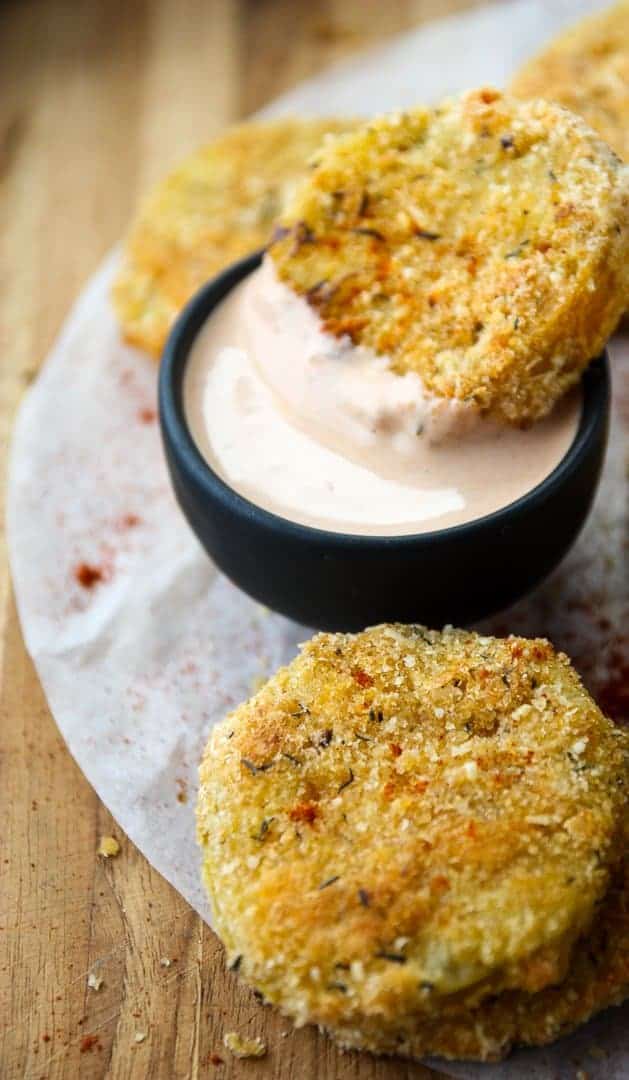 A fried green tomato being dipped in ranch dressing