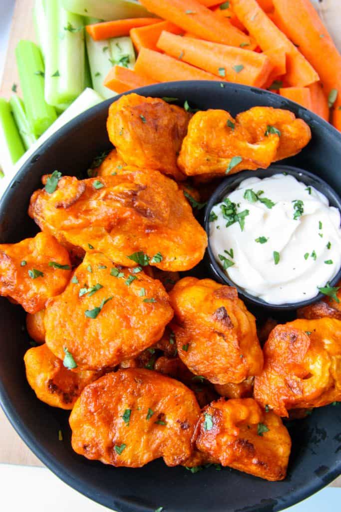 Close up of gluten-free buffalo cauliflower on a black plate with a dish of creamy dip.
