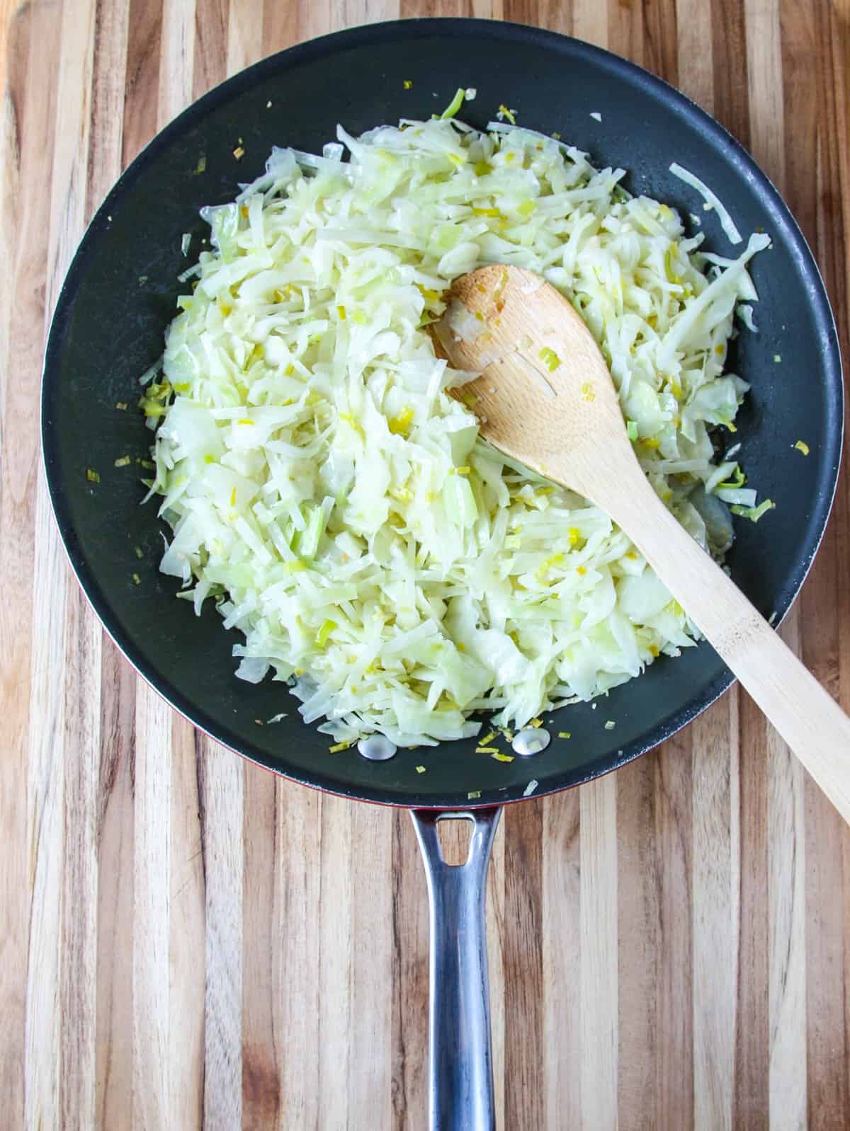 Shredded cabbage and leeks being sautéed in a pan.