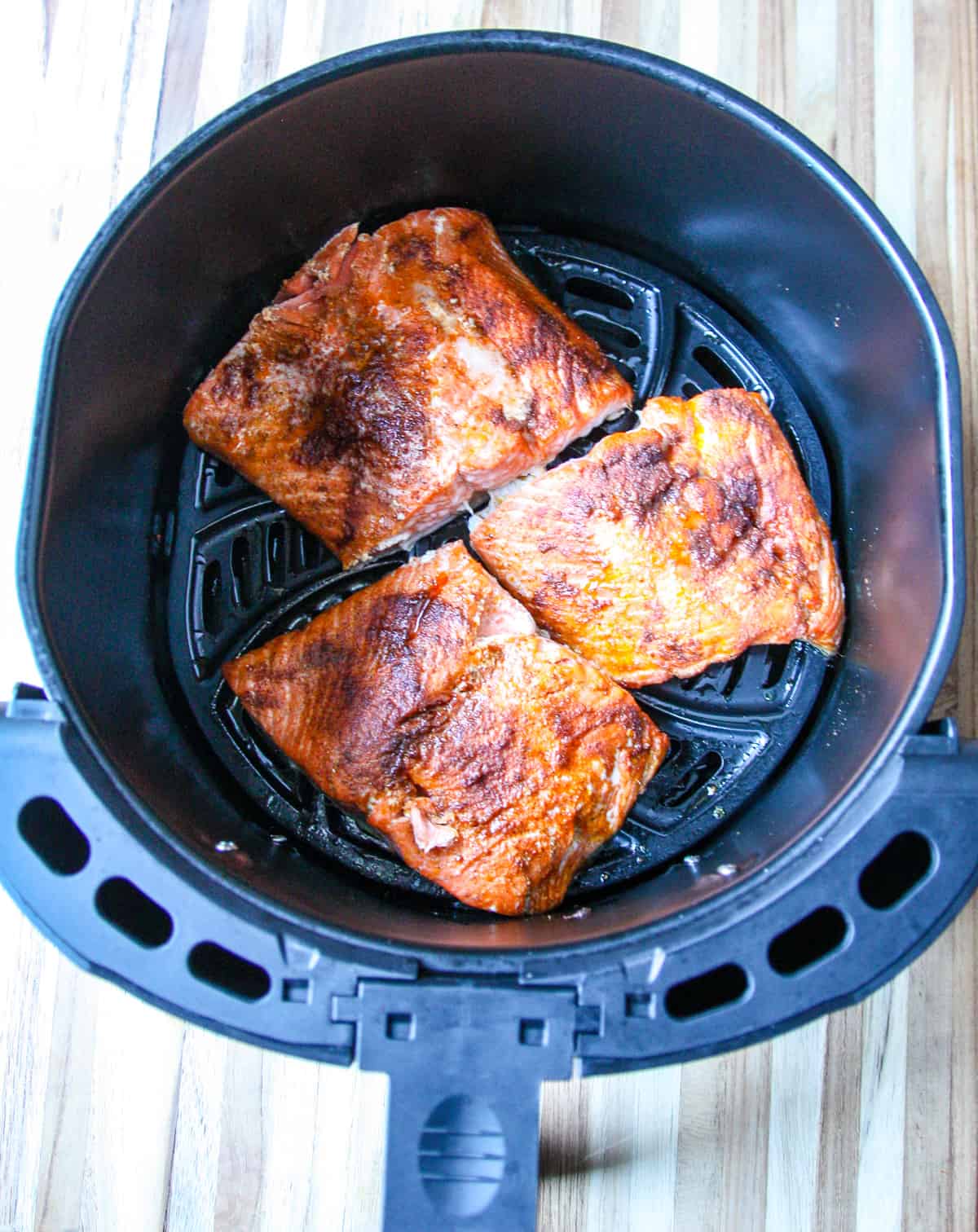 Three cooked salmon fillets in an air fryer basket.