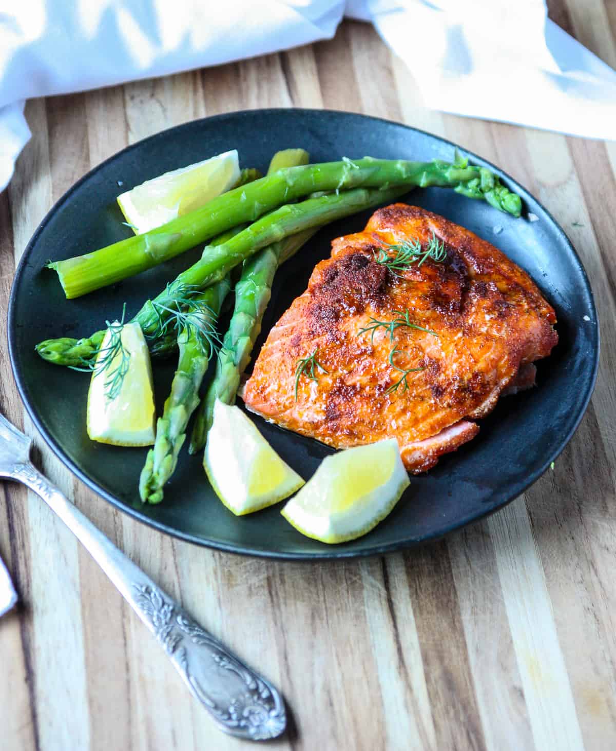 Air Fryer Salmon and asparagus on a black plate with a silver fork.