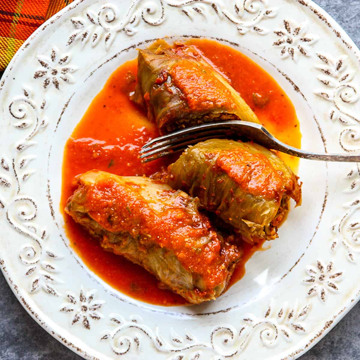 Two cabbage rolls on a plate, one being cut in half with a fork.
