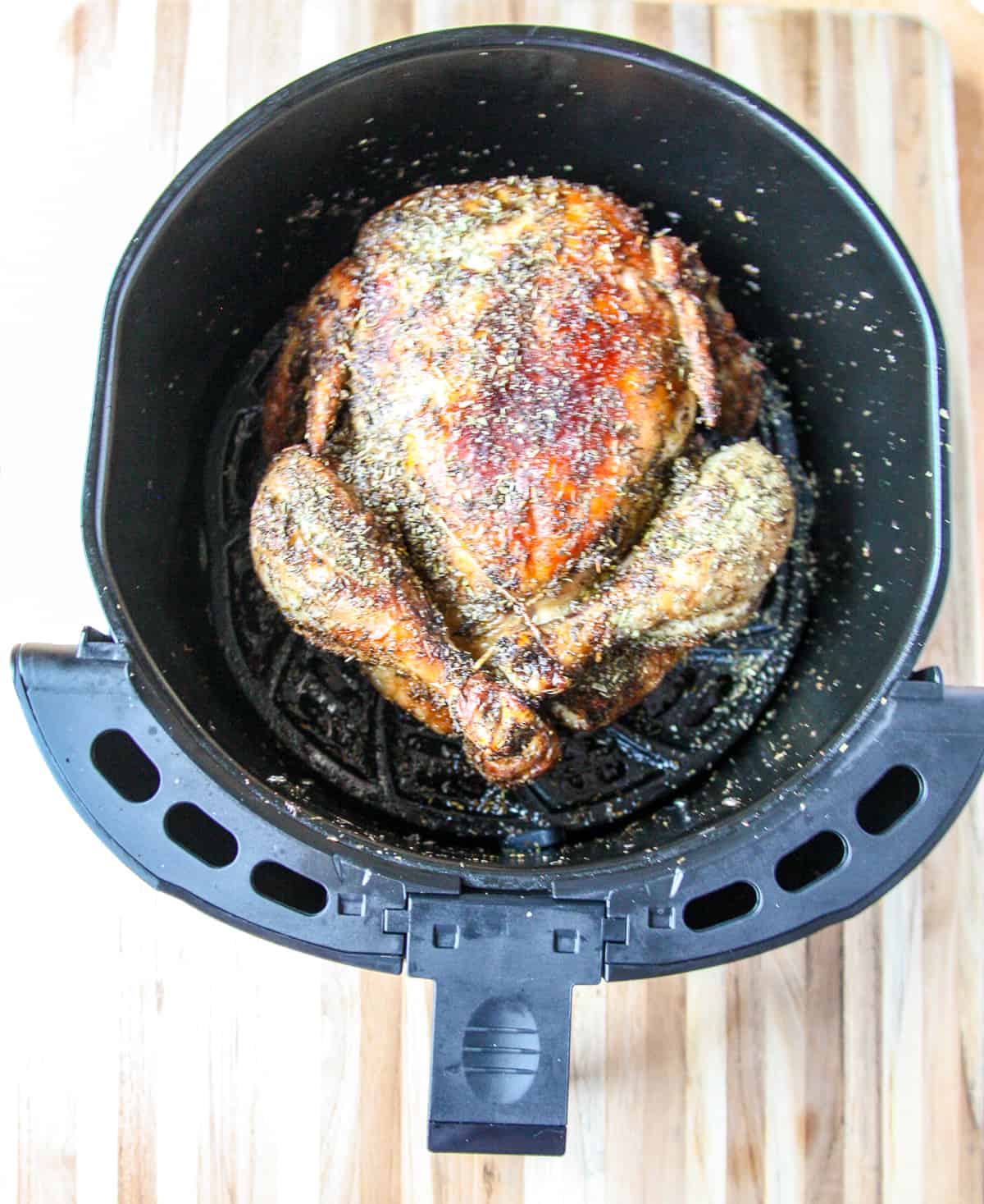 A fully cooked air fryer whole chicken still in the air fryer basket.