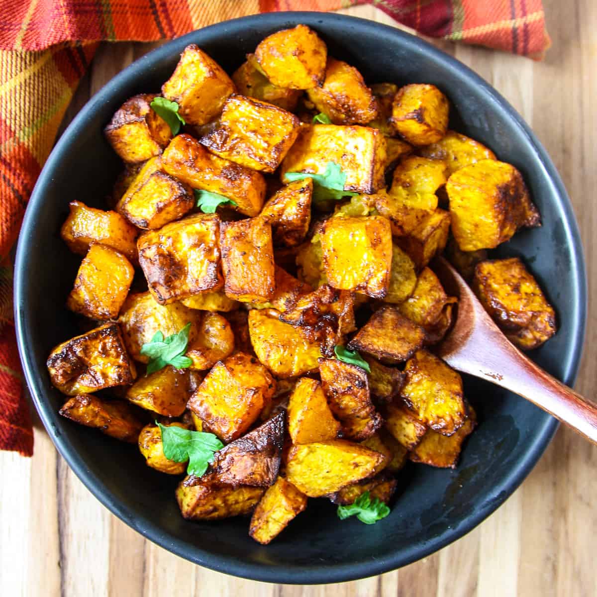 Air fryer butternut squash cubes in a bowl with a wooden spoon.