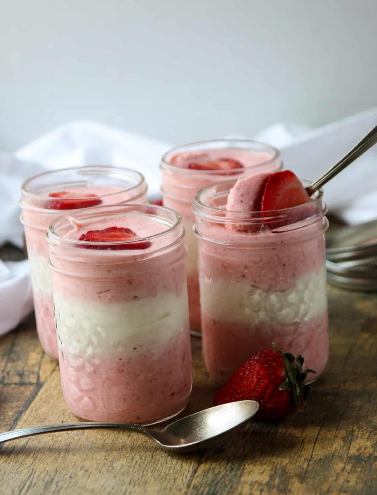 Four jars of pink and white layered mousse topped with strawberries.