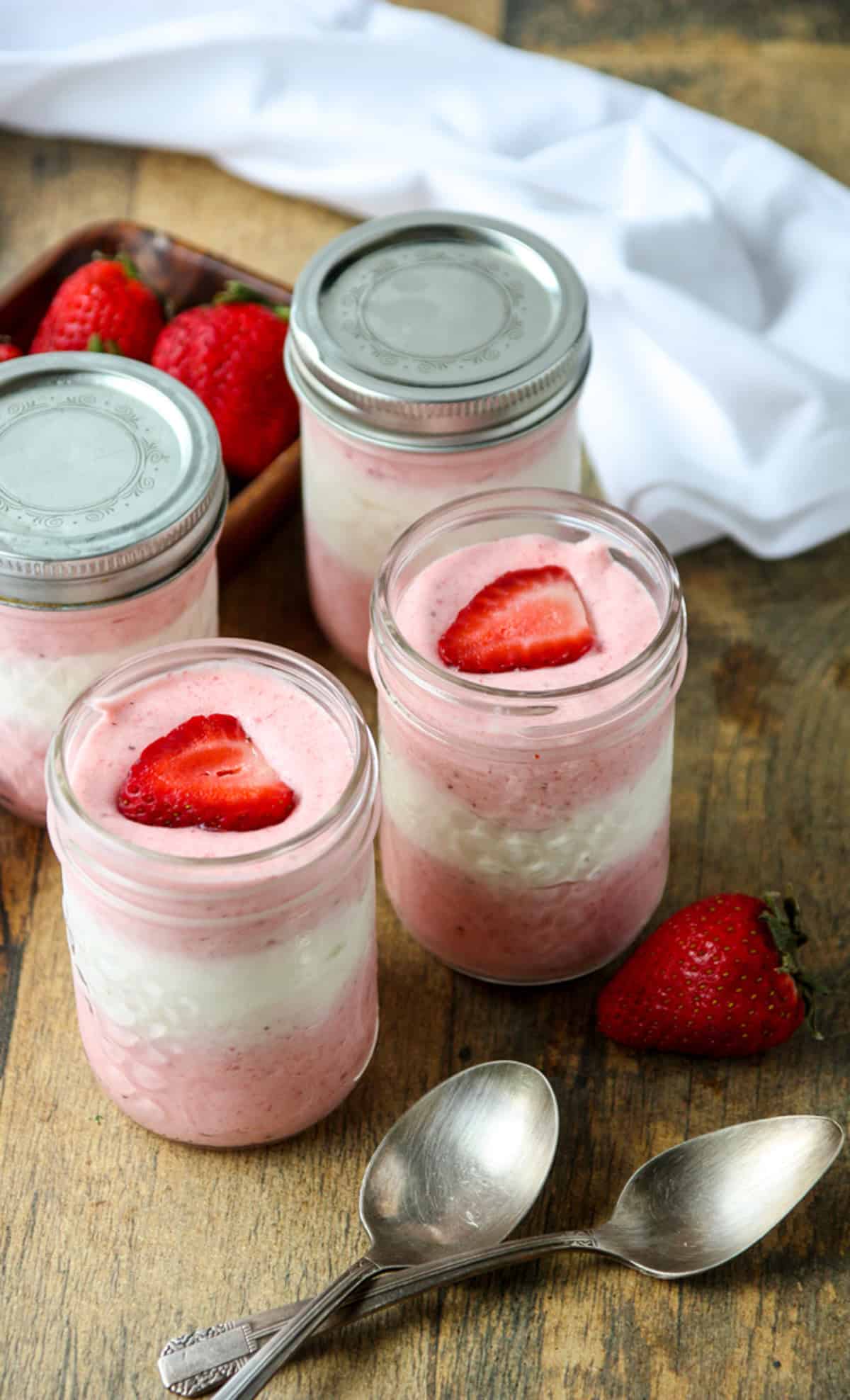 Four small mason jars filled with the dessert, two with lids, and two silver spoons.