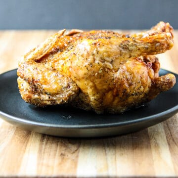A whole air fried Cornish hen on a black plate.