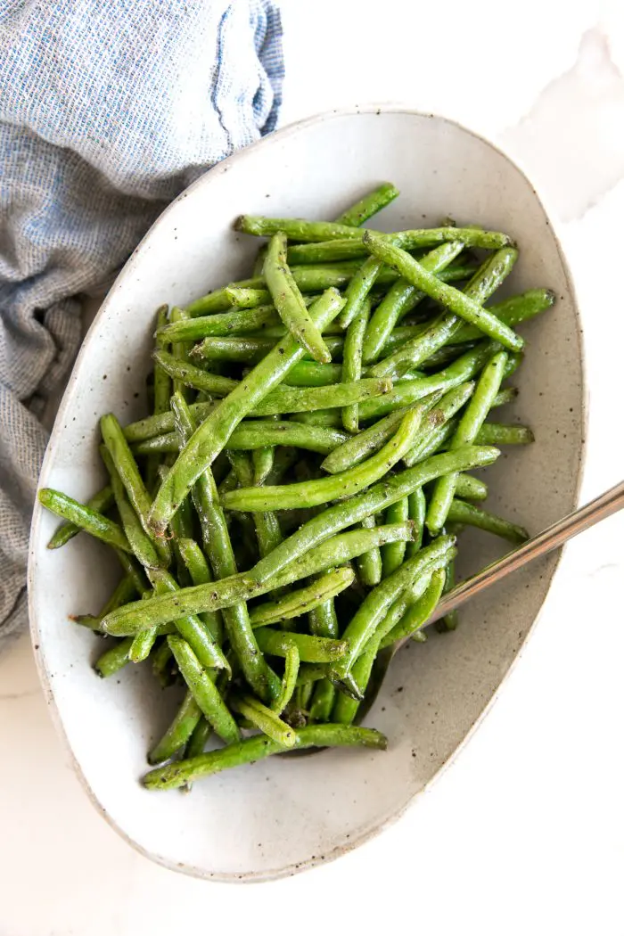 Cooked green beans in a oval shaped white dish.