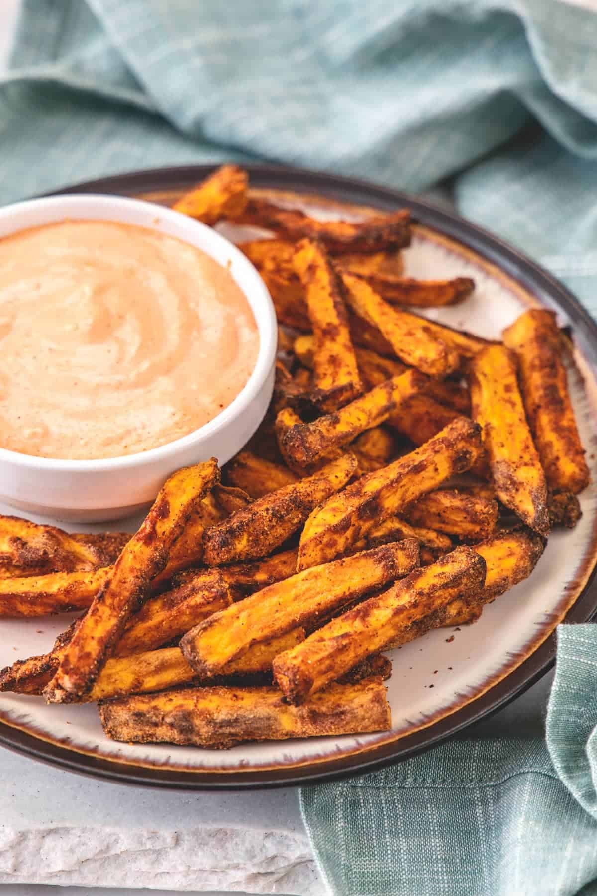 Sweet potato fries on a plate with a dish of dipping sauce.