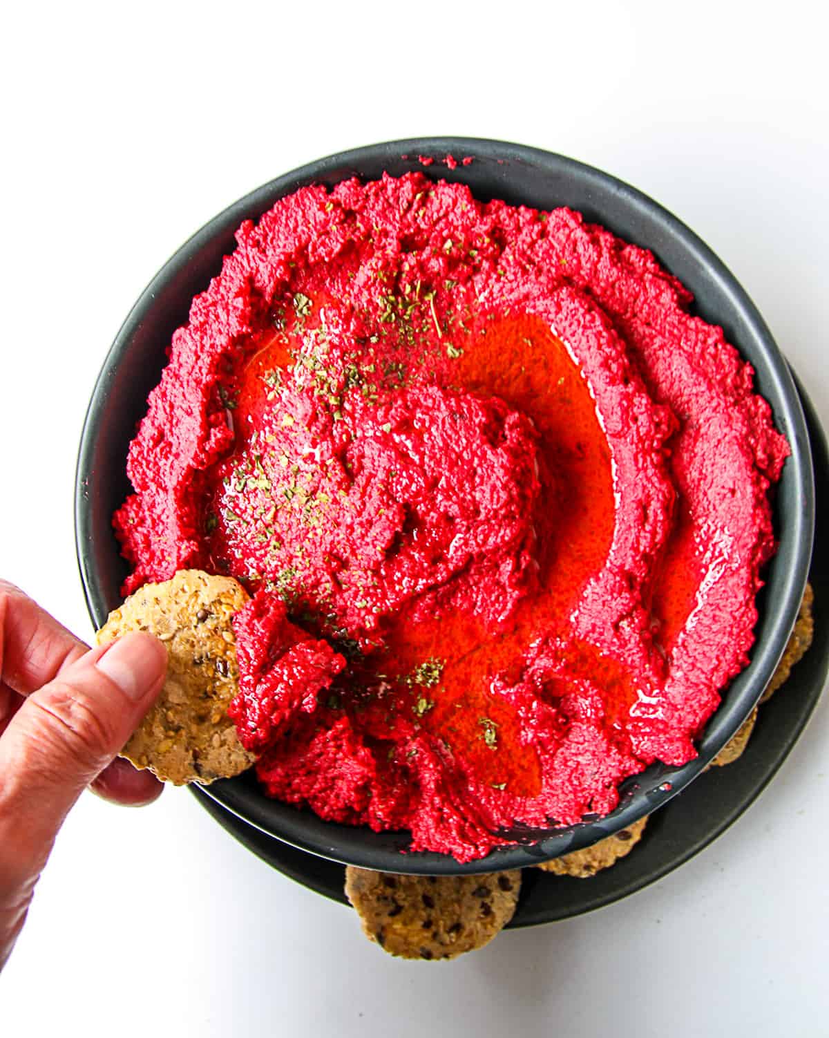 Fingers dipping a cracker into a bowl of roasted beet hummus.