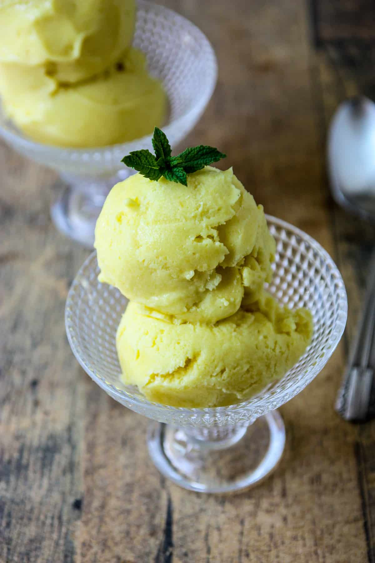 Two scoops of mango coconut ice cream in a glass ice cream dish.