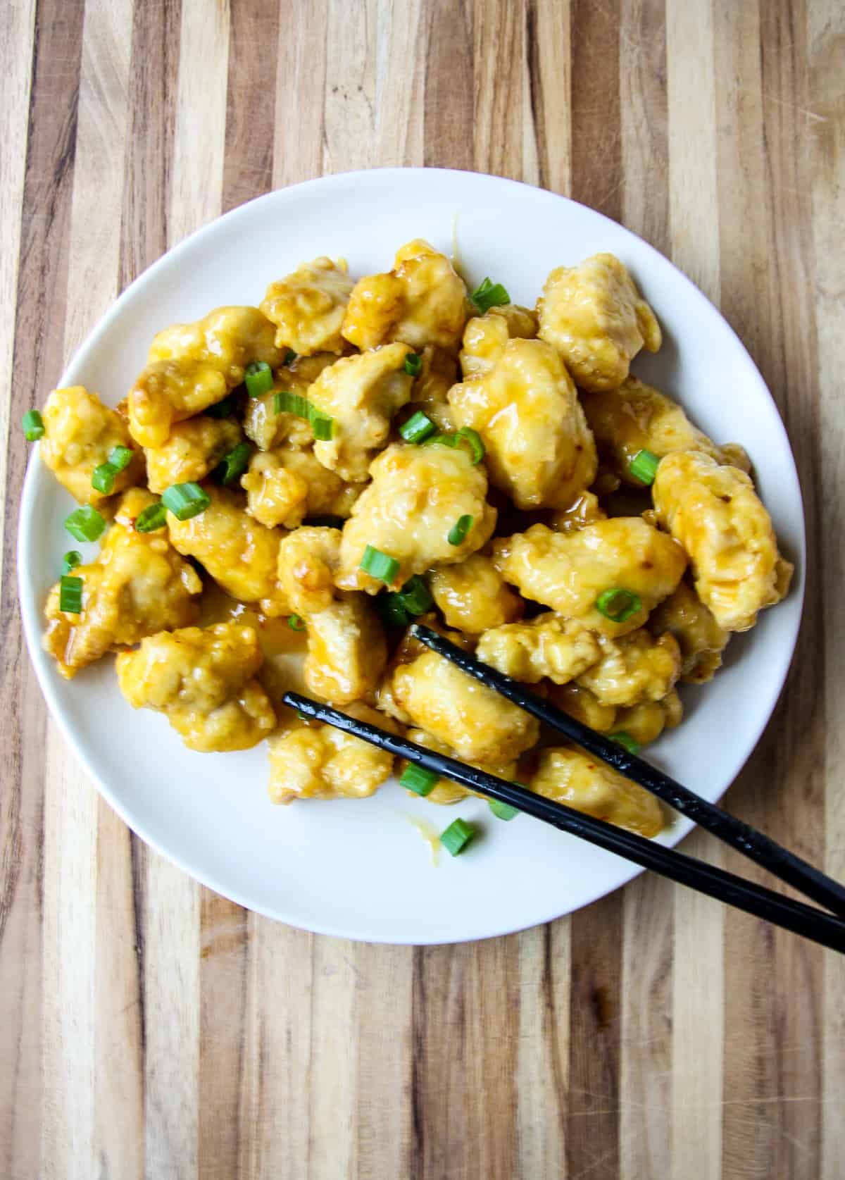 Air fried orange chicken on a white plate with black chopsticks.