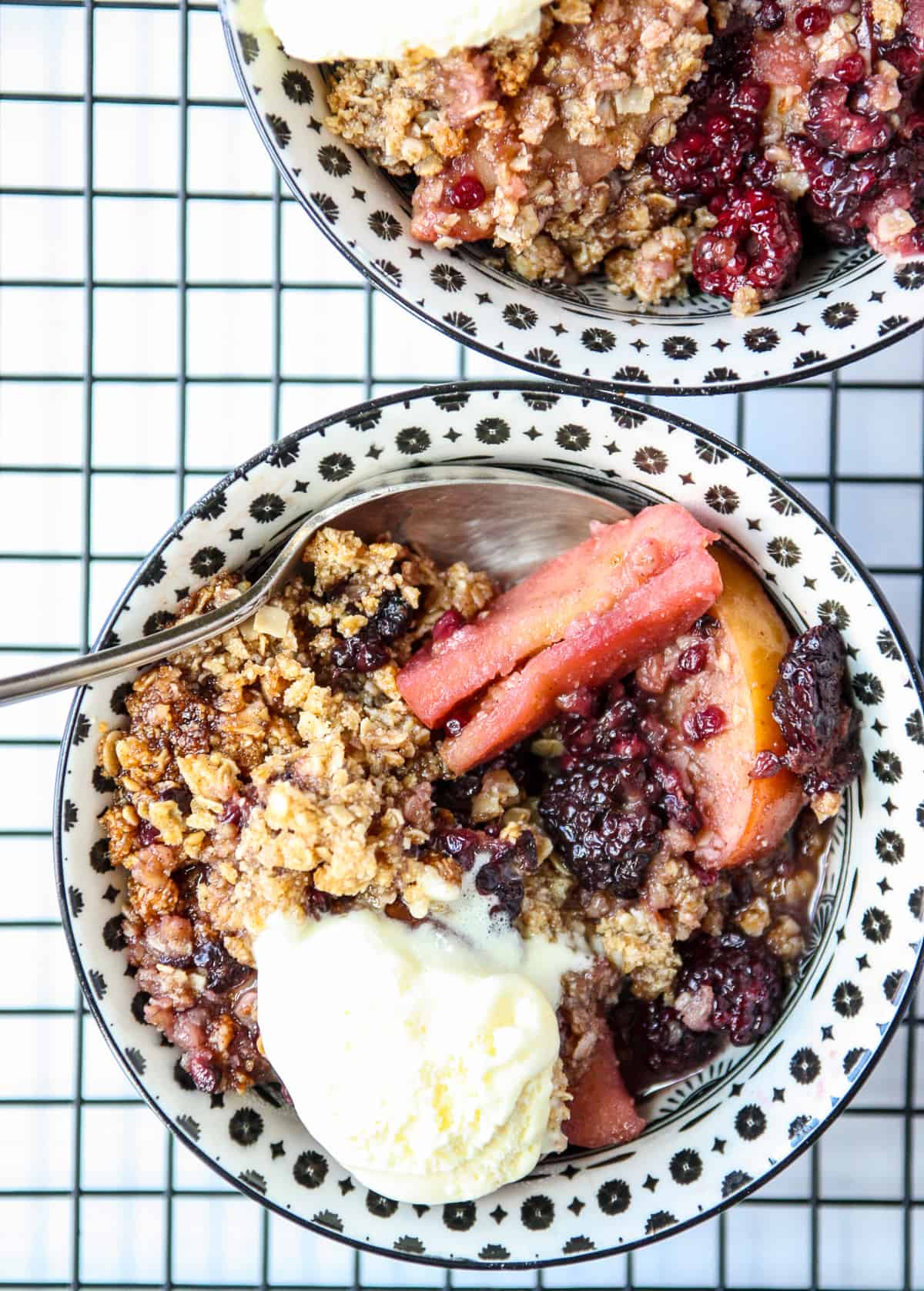 Two bowls of apple and blackberry crumble with silver spoons.
