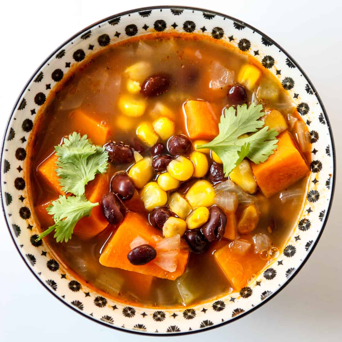 Sweet potato soup with black beans and corn in a black and white bowl.