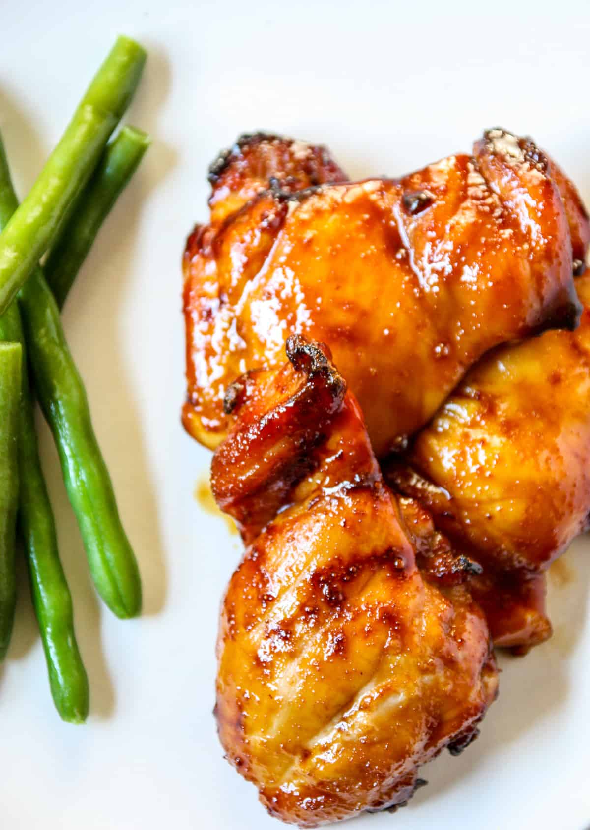Teriyaki chicken alongside green beans on a white plate.