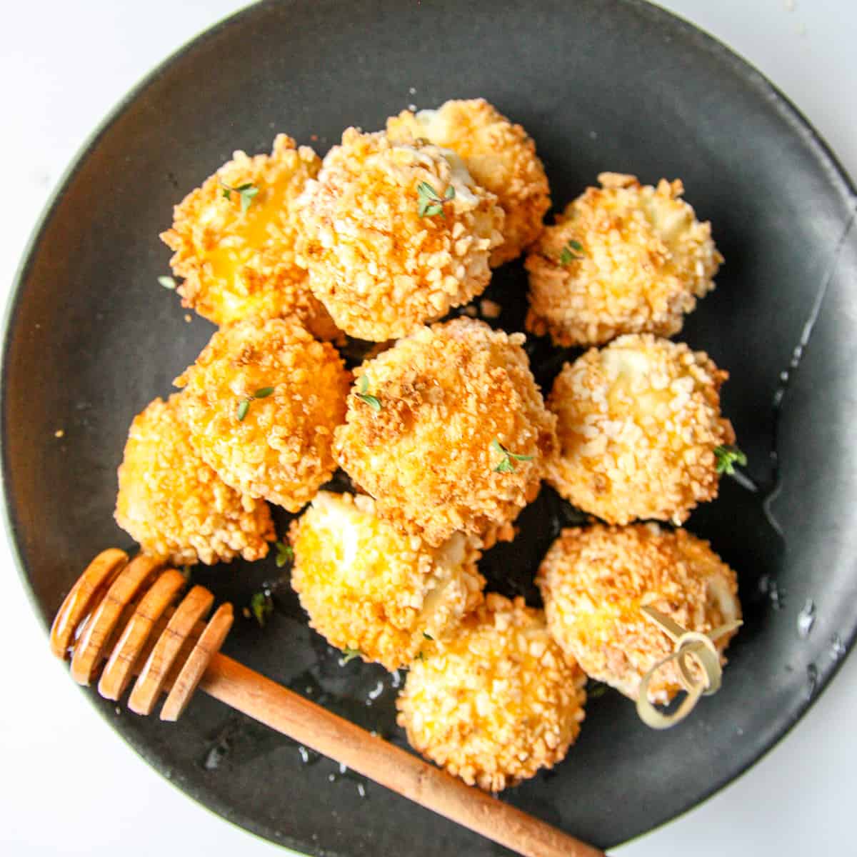 Several fried goat cheese balls on a black plate.