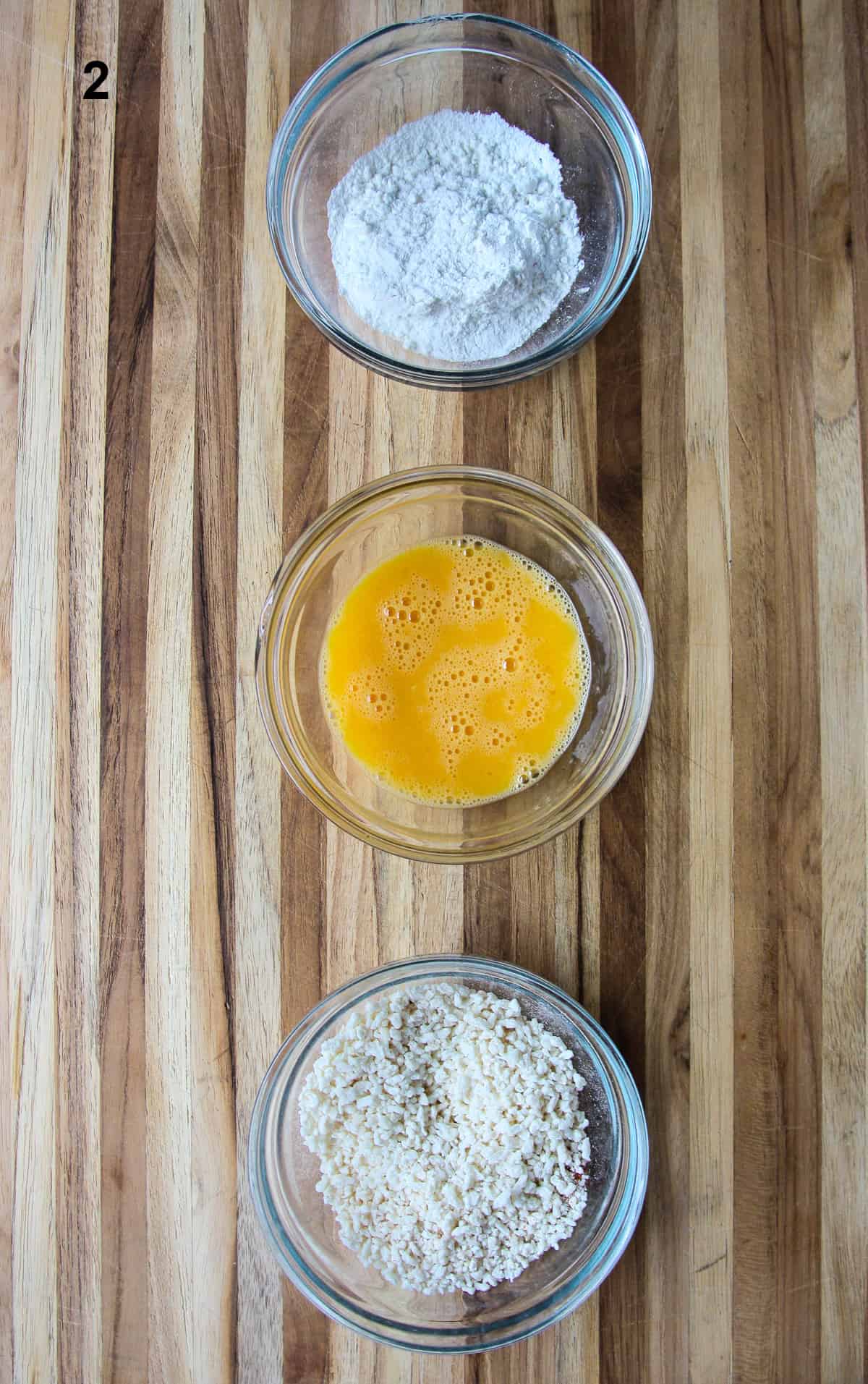 Flour, beaten egg, and breadcrumbs lined up in glass bowls.