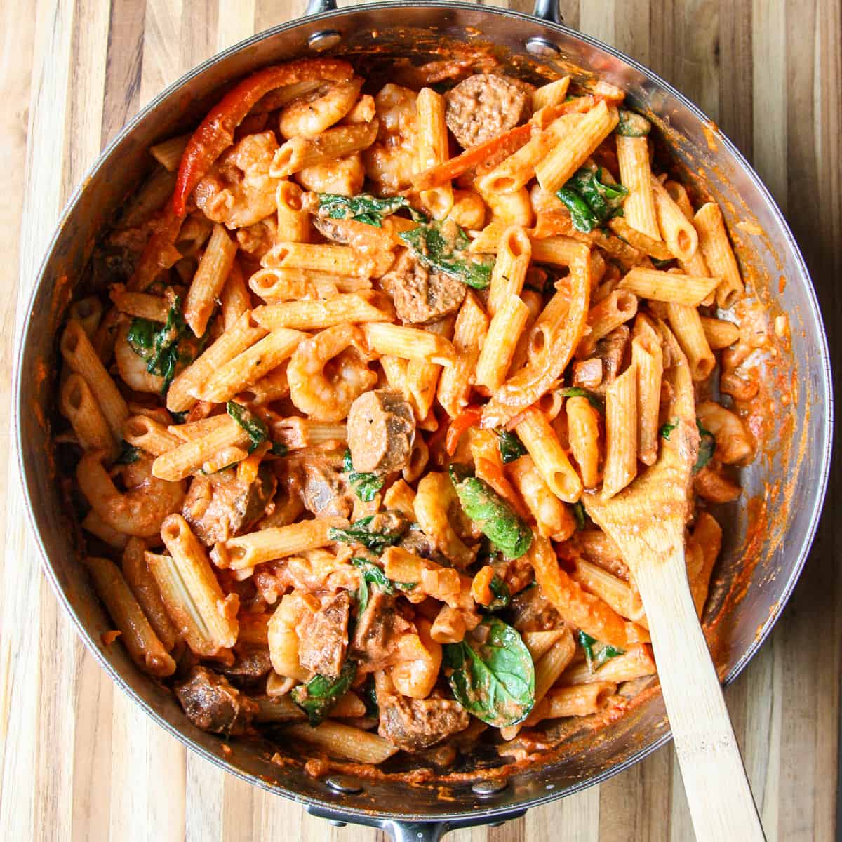 The cooked pasta being stirred into the rest of the ingredients in the pan.