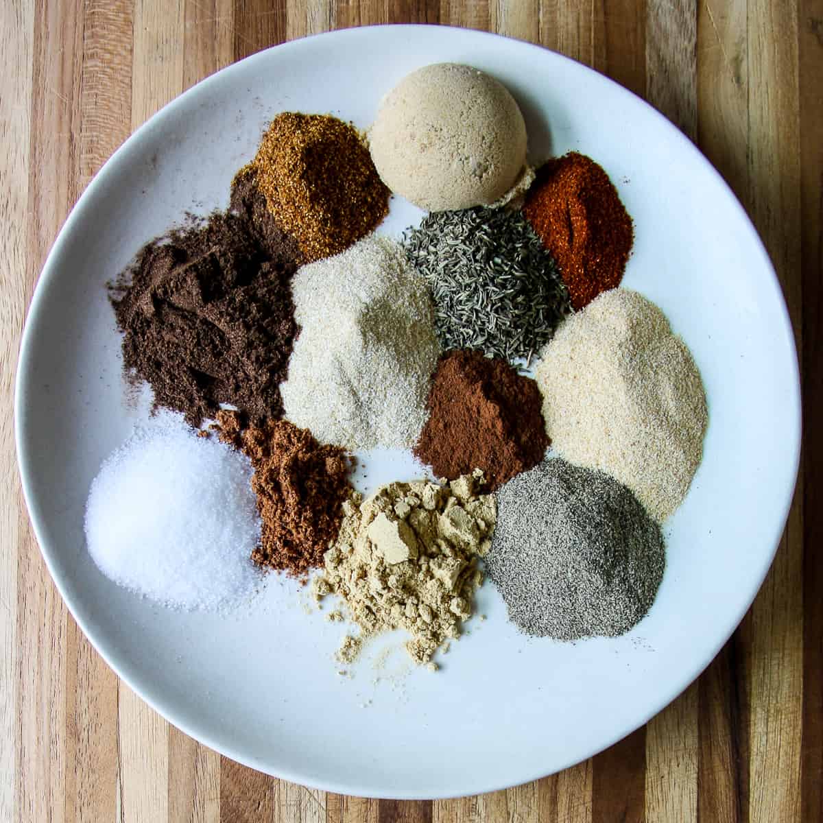 Small mounds of individual spices on a white plate.