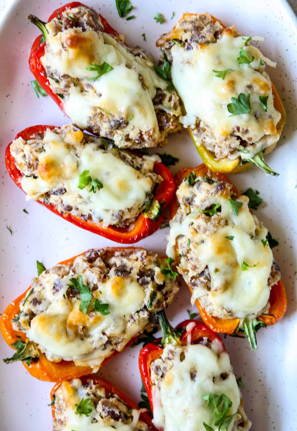 Multi colored sausage stuffed mini peppers on a white plate.