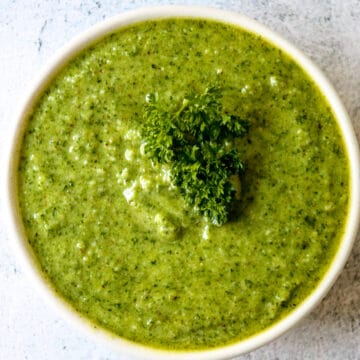 Bright green parsley pesto in a white bowl, garnished with a sprig of fresh parsley.