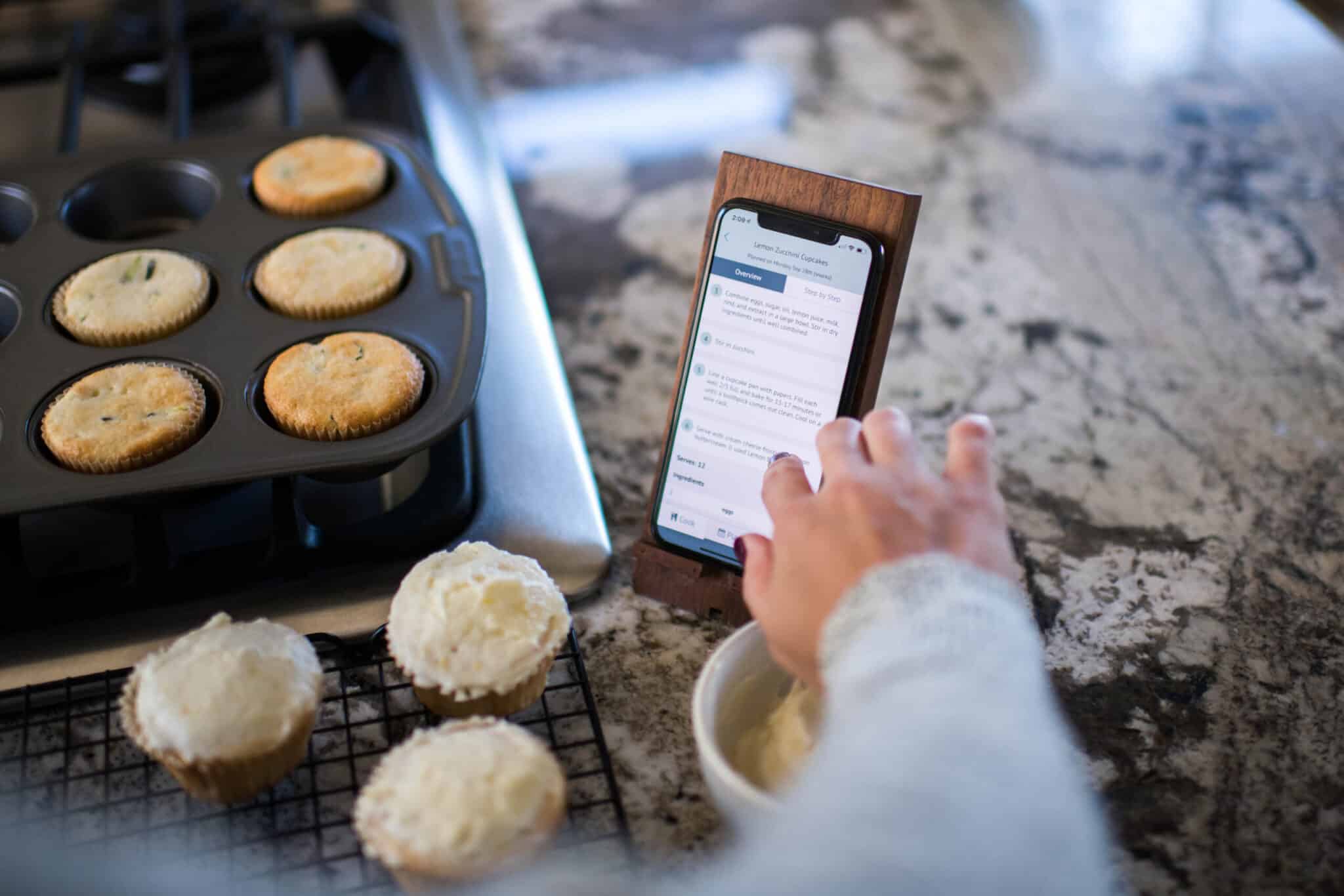 cropped image of a phone on a stand with cupcakes in the background