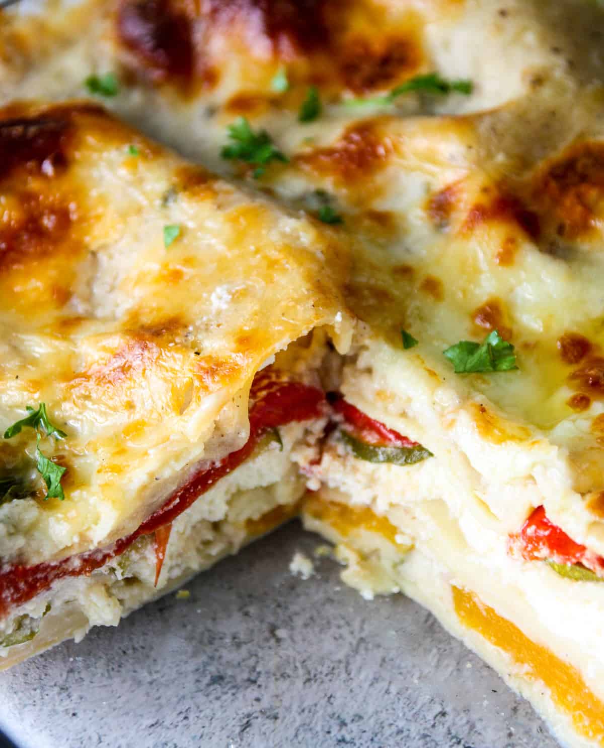 A sliced vegetable lasagna with white sauce showing layers of noodles, cheese, and vegetables.