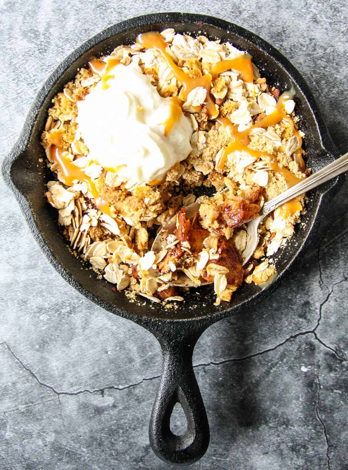 Apple crisp in a black pan with a silver spoon.