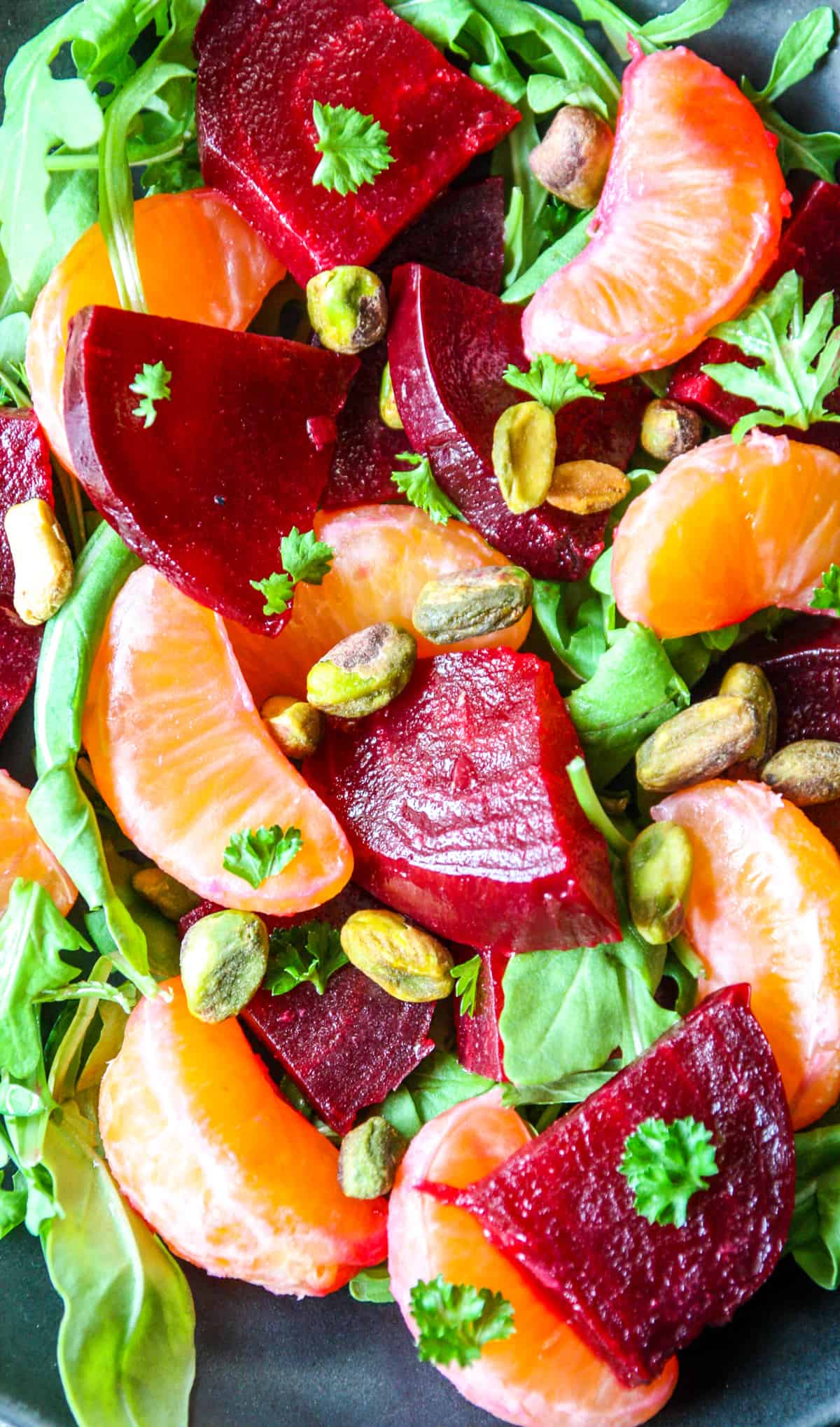 A close up of beet and orange salad with arugula and pistachios.