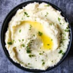 Creamy parsnip puree topped with melted butter, in a black bowl.