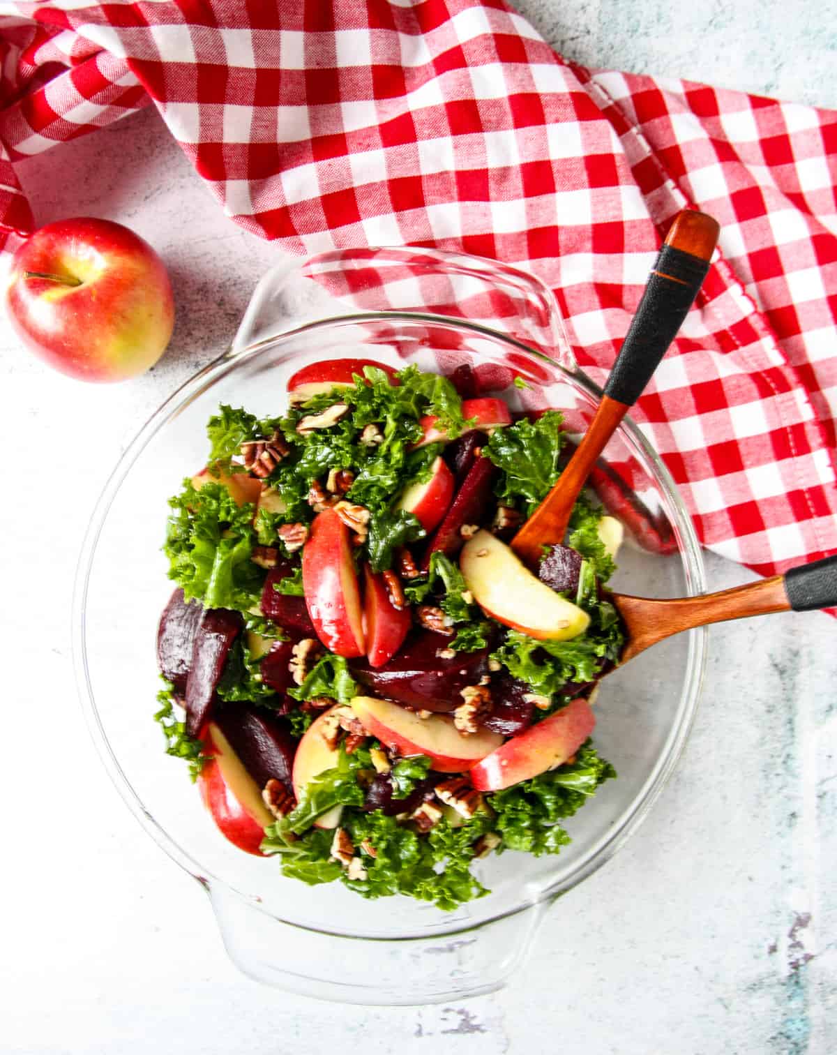 A glass dish filled with kale and beet salad on a stone counter top beside an apple.