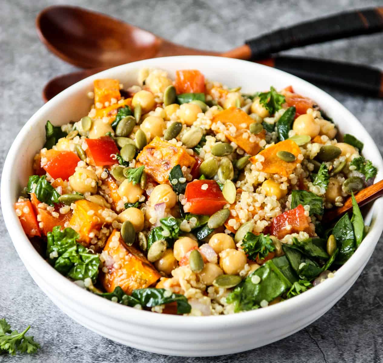 Sweet potato quinoa salad in a white bowl, with wooden salad spoons in the background.