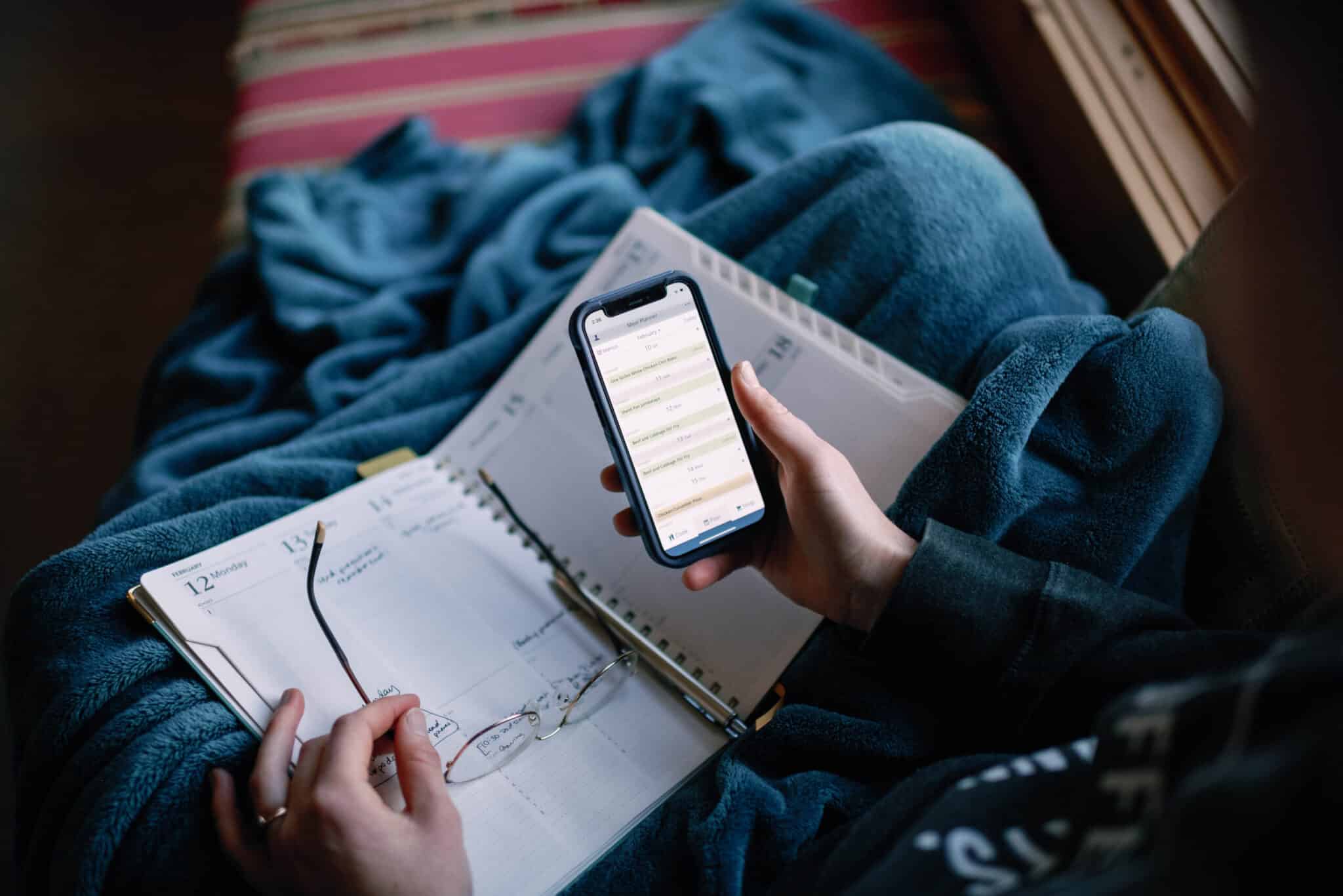view over the shoulder of a woman looking at her phone with a planner in her lap